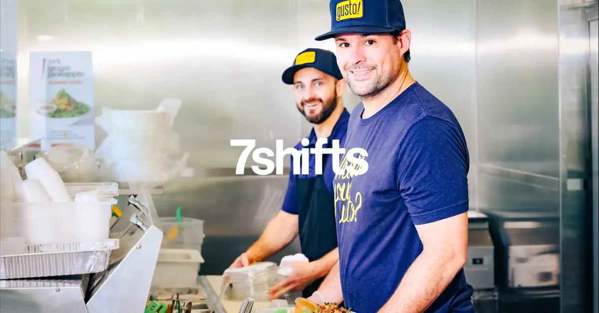 Two back of house workers in restaurant kitchen smiling, 7shifts logo overlay on top