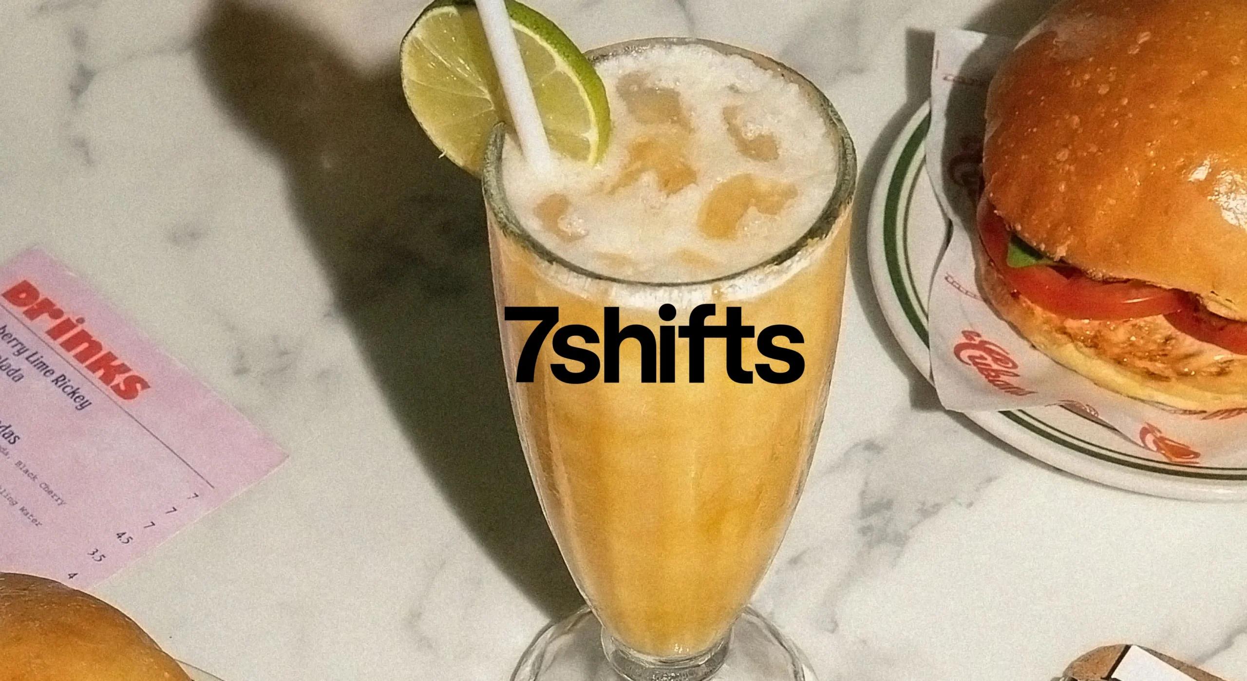 Image of cocktail on restaurant table with burger and drinks menu, 7shifts logo on top