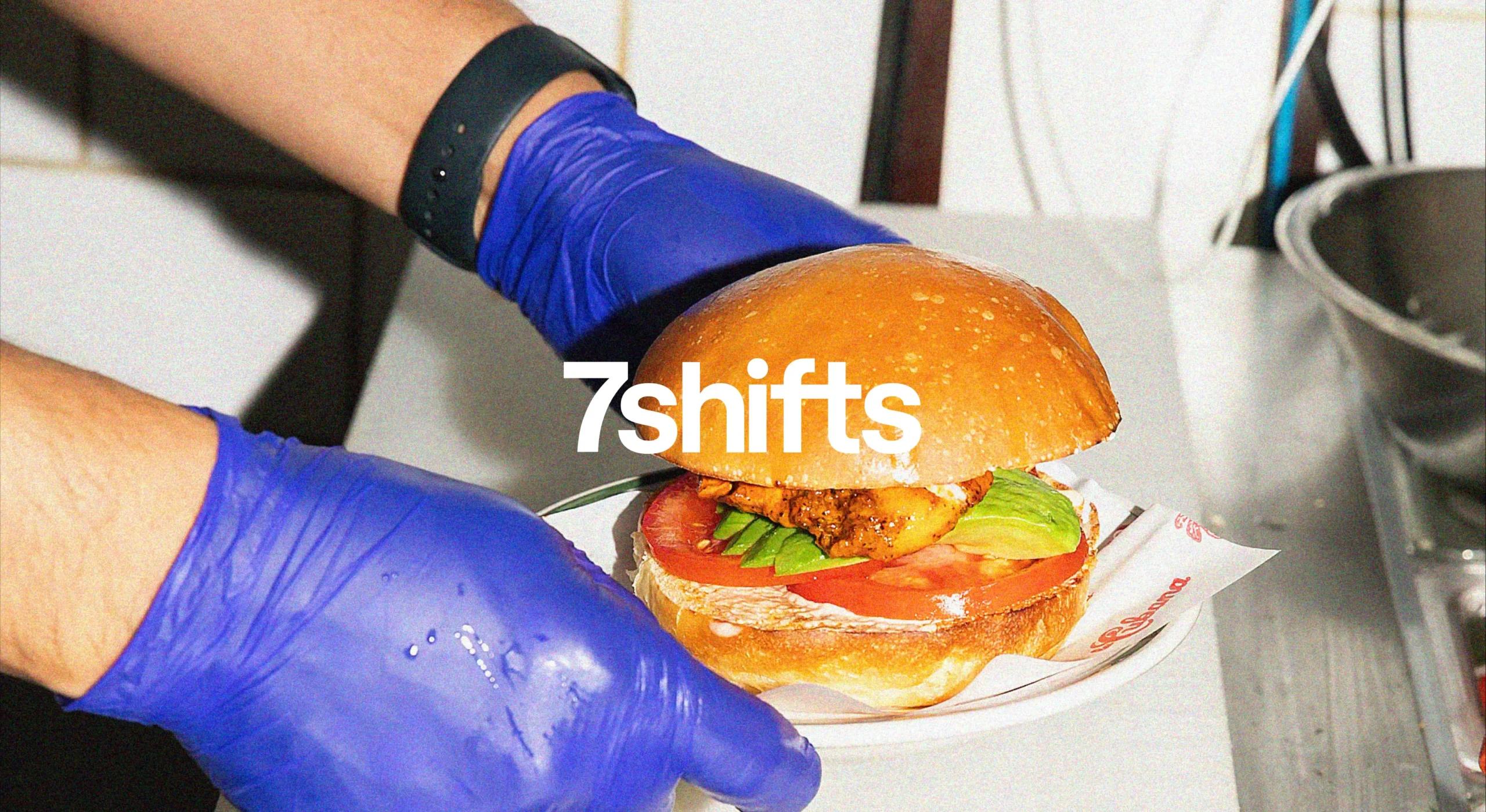 Photo of back of house worker plating a burger in a restaurant, white 7shifts logo overlaid on top