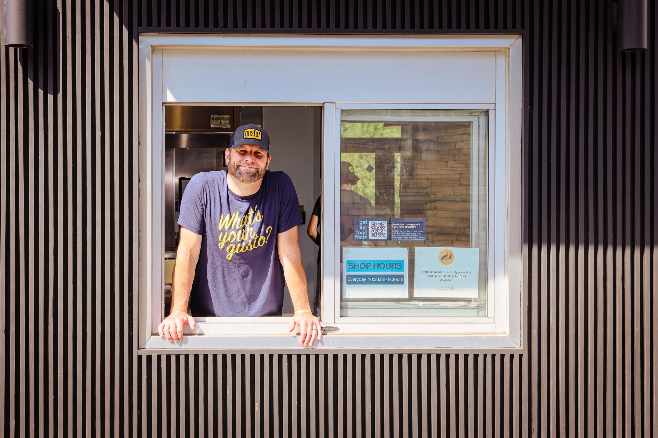 Owner of gusto! restaurant leaning out of the drive-thru window smiling