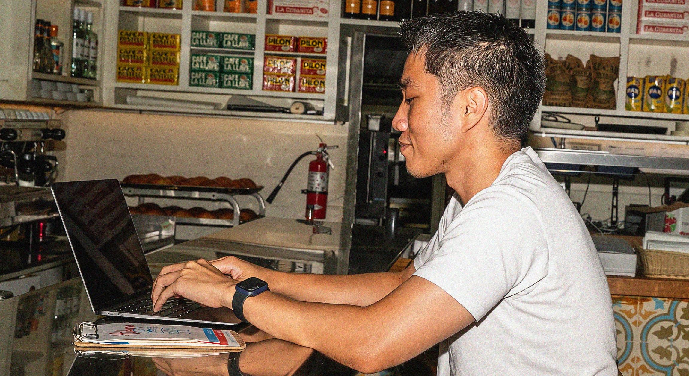 Restaurant employee tying on laptop at counter.