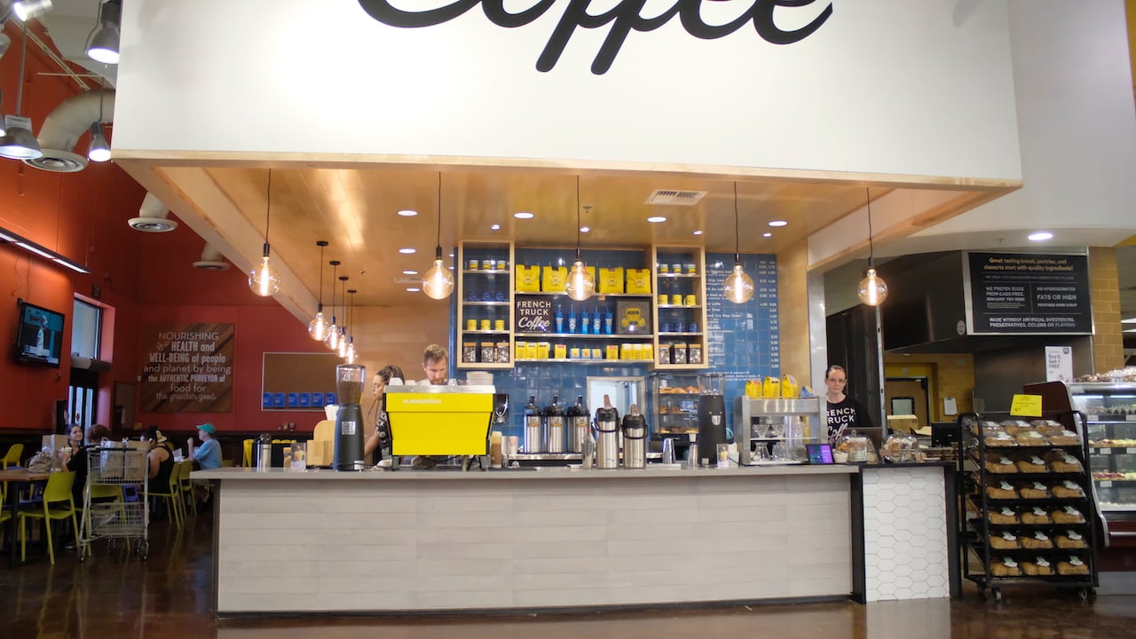 Cafe with baristas serving customers in bright setting.