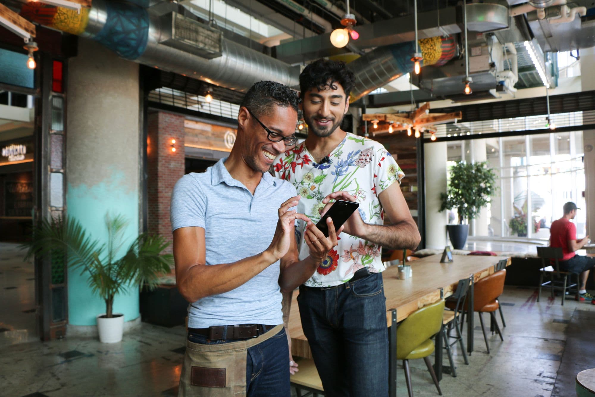 Two people smiling, looking at a phone in cafe.