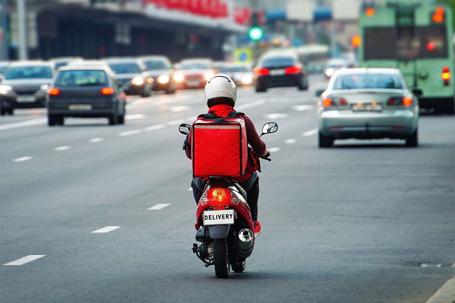 Delivery person on scooter in traffic, urban street.