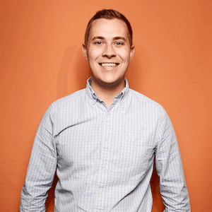 Smiling person in checkered shirt against orange background.