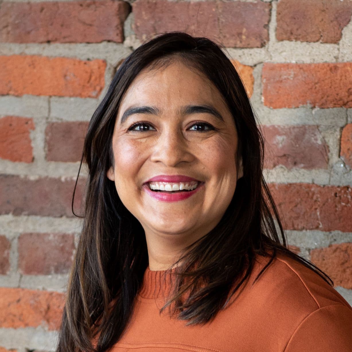 Smiling person in front of brick wall