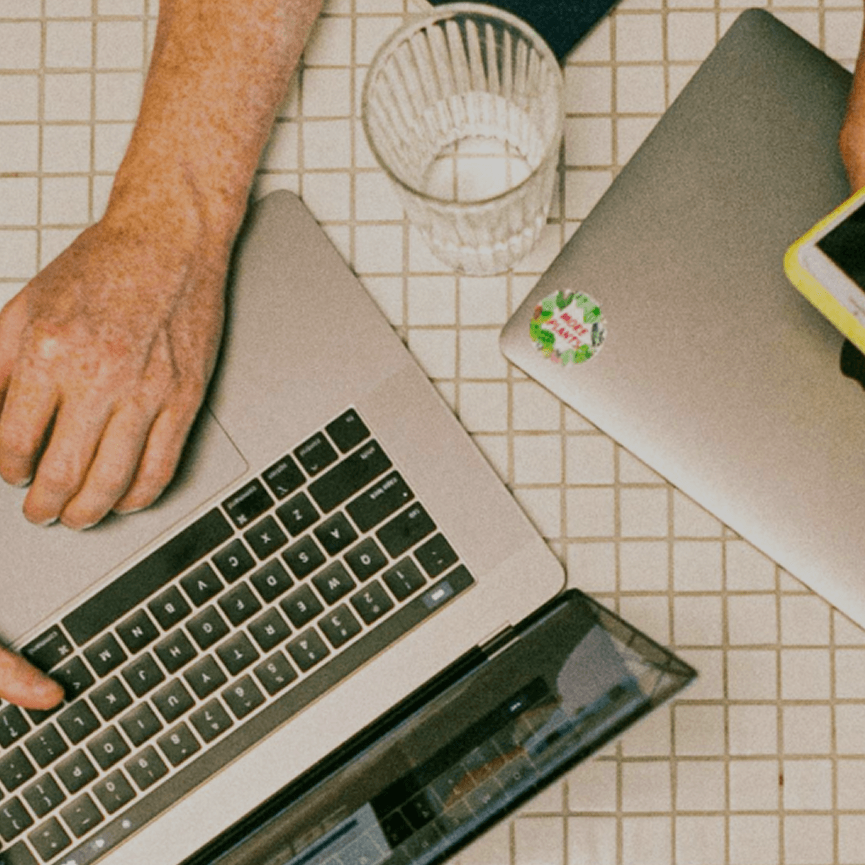 Person typing on laptop beside person scrolling on phone
